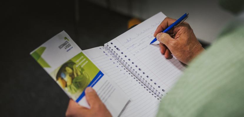 Person writing on a notebook holding a Interreg Europe brochure Person writing on a notebook holding a Interreg Europe brochure