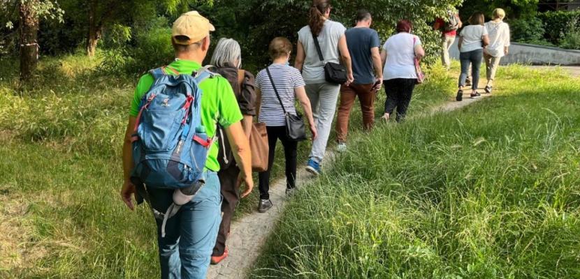 City of Trails Reggio Emilia People walking in line on a trail, immersed in greenery, with hats and backpacks.