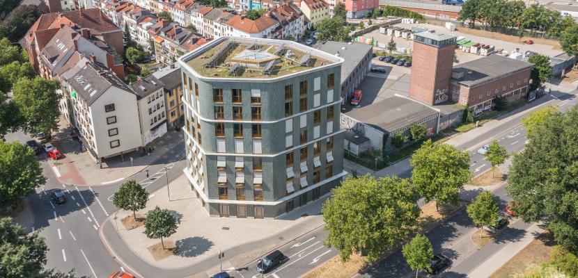 Green flat roof at the Green House Bremen The picture shows a hexagonal, green-colored residential building with a green flat roof. The green roof is designed to be insect-friendly, with flowering plants and dead wood for nesting.