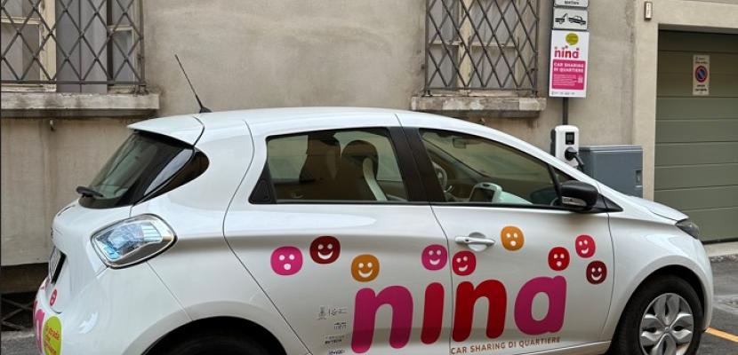 NINA Neighbourhood car sharing NINA car sharing vehicle, a white car with a pink and red NINA logo on the side and the words ‘neighbourhood car sharing’, parked in a dedicated car park indicated by a sign.