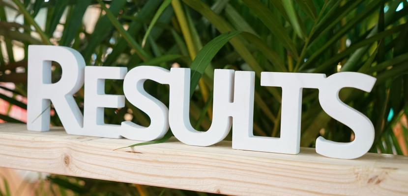 White wooden hashtag spelling out Results placed on a wooden shelve with a plant behind it