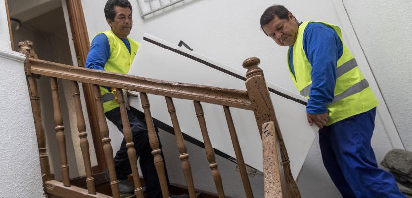 Two men lowering a fride by the stairs.
