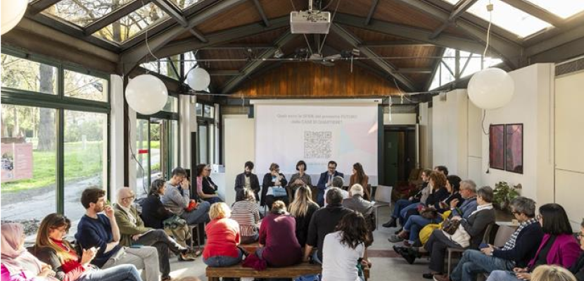 Neighbourhood Houses Group of people meeting in a building with wooden beams and large windows, looking at a screen with a QR code to collect inputs
