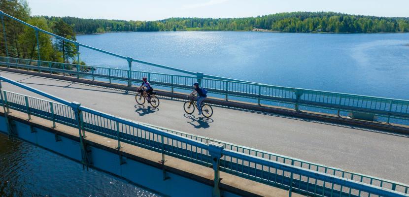 Cyclists on the bridge Lake scenery on the bottom a long bridge where two cyclists heading to the left