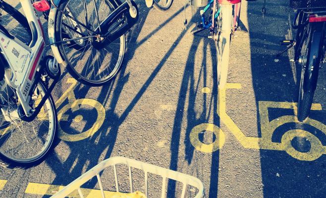 The photo shows sections of bicycles and their shades on a storage point for bicycles and e-scooters. The storage point is labelled with a pictogram for bicycles and e-scooters.