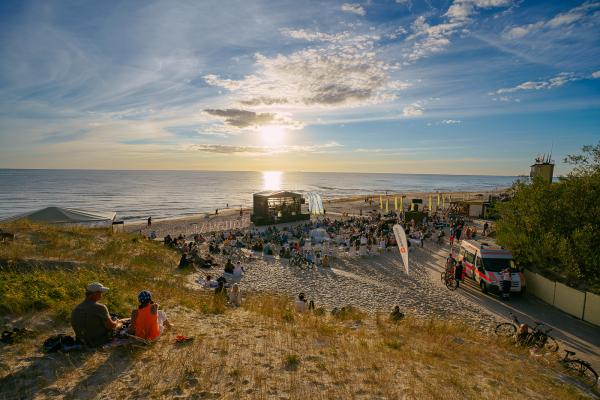 A concert on a beach with a group of people sitting on the sand