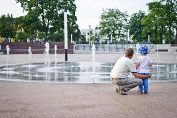 A man and child from the back standing in front of a fountain