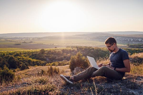 man using a laptop on a cliff