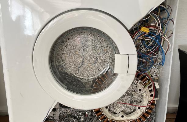 A close up of a washing machine filled with cables and other discarded parts of electronic devices