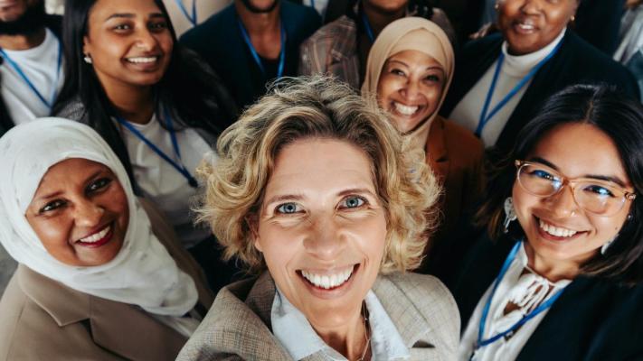 The image depicts a mature woman leading a diverse team with enthusiasm and professionalism