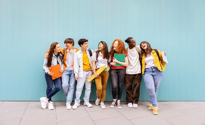 I see a group of happy young people gathered side by side, carrying school bags and exercise books