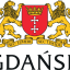 The image shows the coat of arms of Gdańsk, a city in Poland. It features a red shield with a gold crown on top, and two white crosses (specifically the Maltese crosses) positioned vertically in the center of the shield. The shield is flanked by two gold lions, each standing on its hind legs. Below the shield is a ribbon banner with the Latin motto "NEC TEMERE NEC TIMIDE," which translates to "Neither rashly nor timidly." Below the banner, the word "GDAŃSK" is written in bold, capital letters.