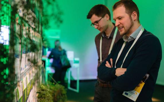 People looking at a green wall with plants and Interreg Europe's projects.