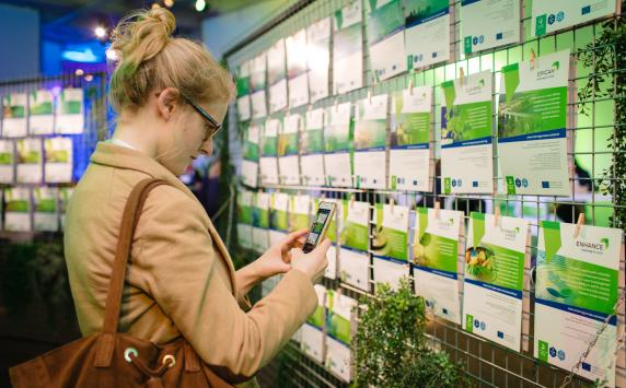 Woman taking a picture of a green wall with Interreg Europe projects on it.