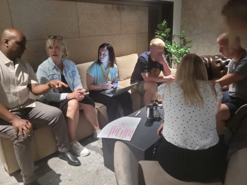 Team members of the FBI4EU project collaborate on strategies for stakeholder engagement, highlighting the importance of inclusive and diverse perspectives in driving successful regional development initiatives. A diverse group of people sitting on sofas and chairs in a cozy room, actively engaged in a discussion about stakeholder engagement. One person is using a laptop, while another is taking notes on a piece of paper with brainstorming ideas.