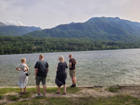 The Danish team from the FBI4EU project enjoys the scenic views of Lake Bohinj, reflecting on the day's insights into sustainable tourism and forest conservation practices. Four members of the Danish team stand by the lakeshore, looking out over the water towards the lush green mountains in Bohinj, Slovenia.