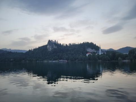 The tranquil evening view of Lake Bled, featuring the historic Bled Castle and a nearby church, provided a picturesque backdrop for the FBI4EU project participants' reflections on the day's activities. A serene view of Lake Bled at dusk, with Bled Castle perched on a hill and a church visible near the shoreline, reflecting in the calm water.