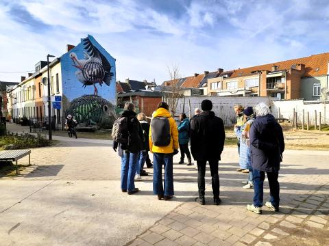 Ghent stakeholder meeting 2 People together outside on a paved square with houses surrounding the square. One of the houses has a mural of a big bird