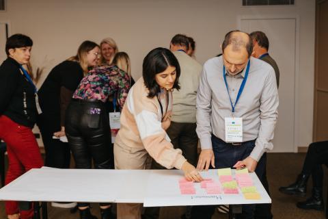 Stakeholder workshop i see 2 people looking at some notes, while behind there others