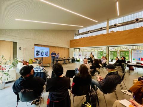Participants in the participatory path to neighbourhood houses meet in a room, two people are presenting using slides