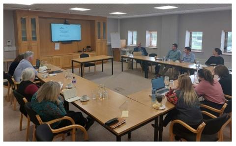 Stakeholders discuss current and next work of the project People seated around a meeting room table