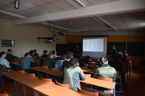 therevare people, chairs, desks, a screen and and a blackboard