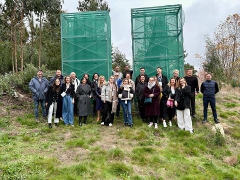 Project Life Nieblas on site visit A group of people standing in the forest, in front of 2 green structures