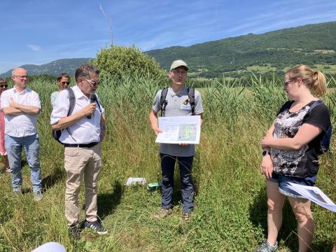 Wetland restoration site, Ruffieux, France. People standing on a green hay field and listening presentation by a man.