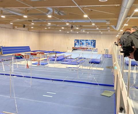 Gymnastics hall built from CLT (Cross Laminated Timber) in Kuortane OTC. A large gymnastics hall with a blue floor and various gymnastics apparatus, and a spectators gallery.