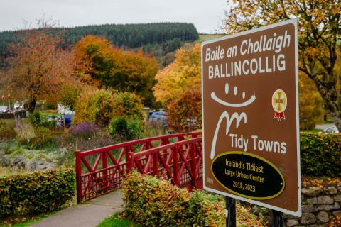 Welcome sign to Ballincollig with trees and bridge in background
