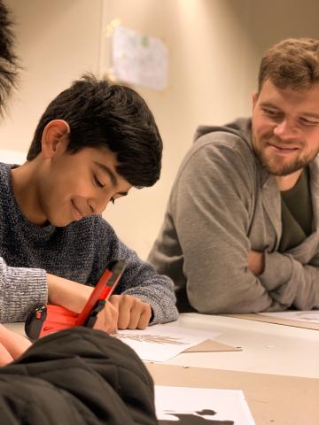 An adult supervising a child working on a crafting activity. 