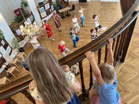 Children watching a group of elderly individuals partake in physical activity from an indoor balcony. 