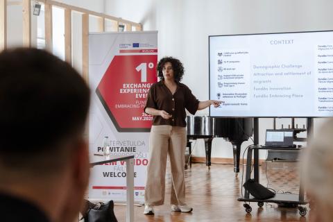 Presentation by Fundão Migration Centre during Involvim event. A woman, representing the Fundão Migration Centre, gives a presentation during the Involvim study visit. She stands beside a large screen displaying key context points about innovation and migration in Fundão.