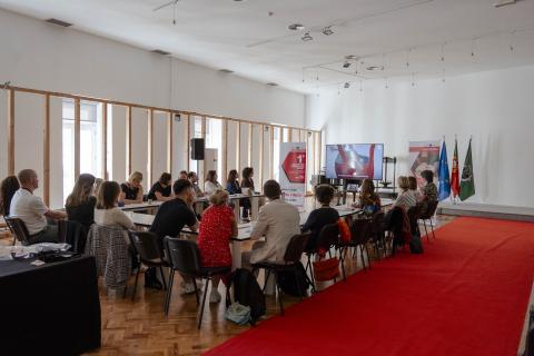 Involvim project partners meeting in Fundão, Portugal. The image shows a group of people seated in a conference room during an Involvim project meeting. A screen displays a presentation, with banners and flags (EU, Portugal, and a local flag) in the background. The setting is formal and collaborative.