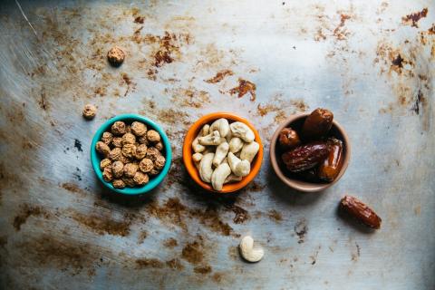 Bowls of Tiger Nuts, Cashew Nuts, and Dates on a Rustic Surface Three bowls on a rustic surface, filled with tiger nuts, cashew nuts, and dates.