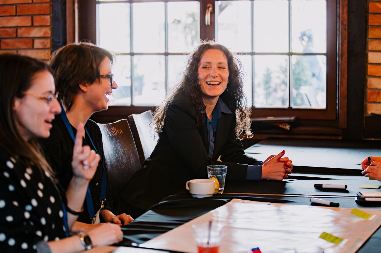 Three women discuss around a table at Europe, let's cooperate! 2025