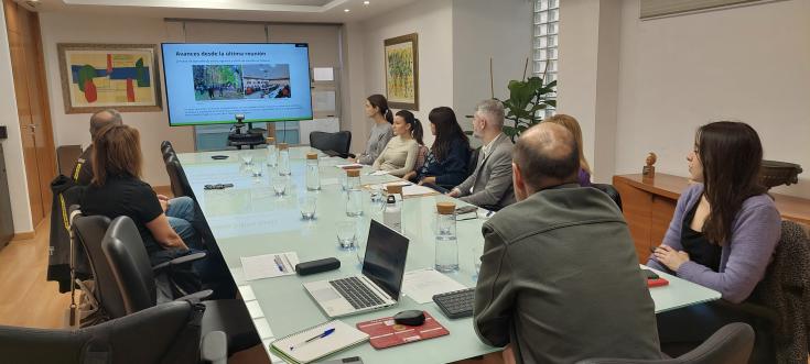 A group of adults sit around a table and look at a screen with slides