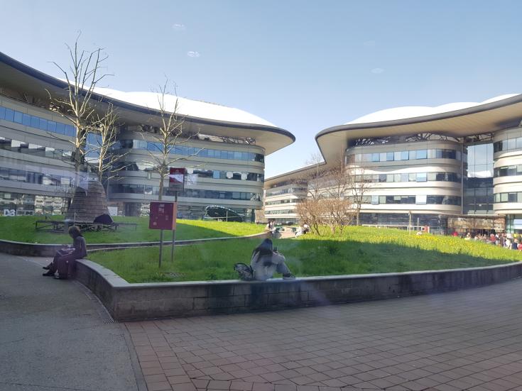 Modern wave-shaped buildings around courtyard with grass and a few people