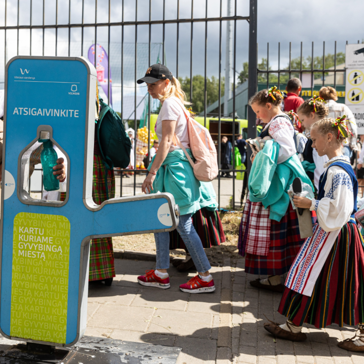 People in regional costumes passing by a mobile water fountain.