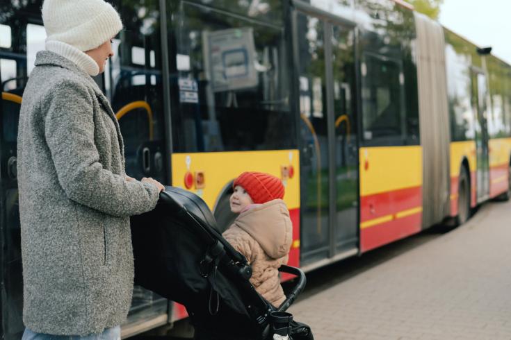 Mother with baby carriage getting into a bus on the station Woman and child in buggy with a bus in the background