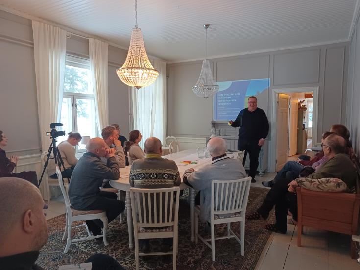 Men in sweaters sit around a round table listening to the presentation.