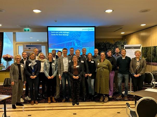 Around 20 people are standing in front of a presentation screen