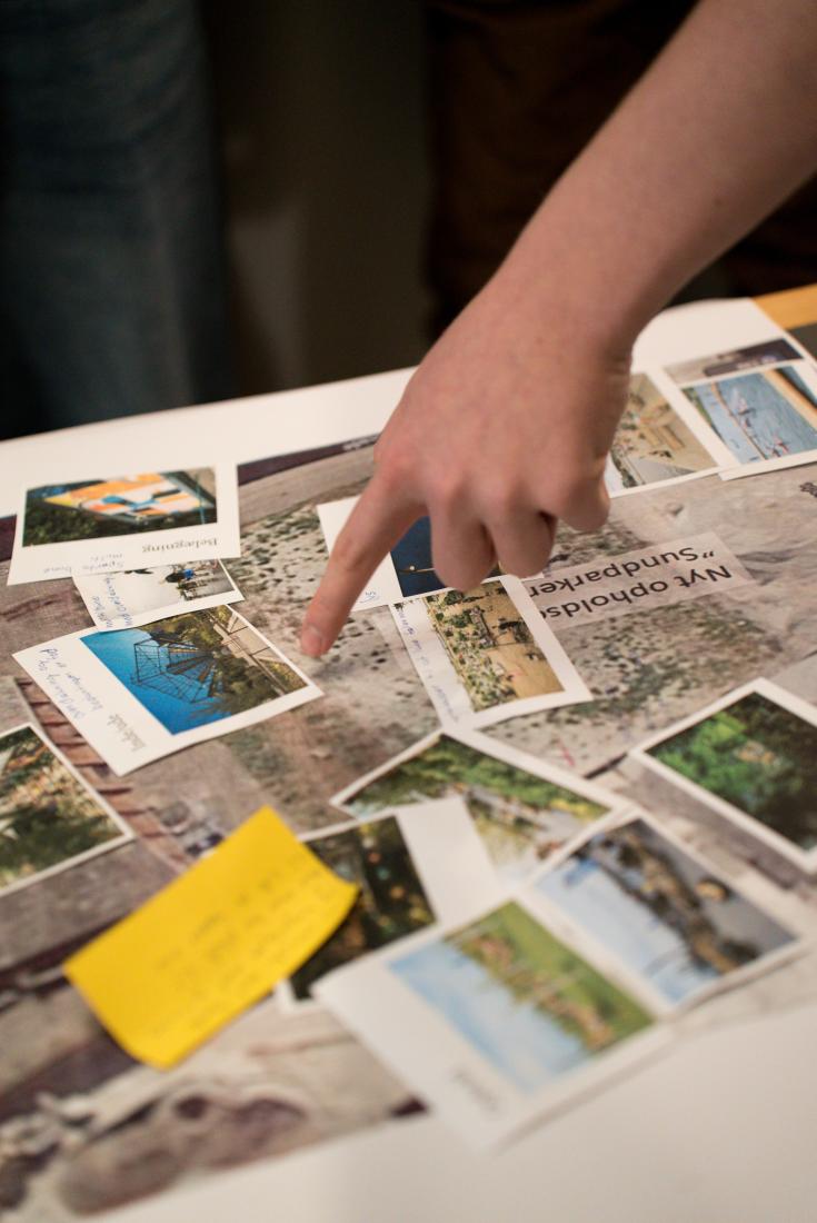 A finger points at some photographs spread out on a table.