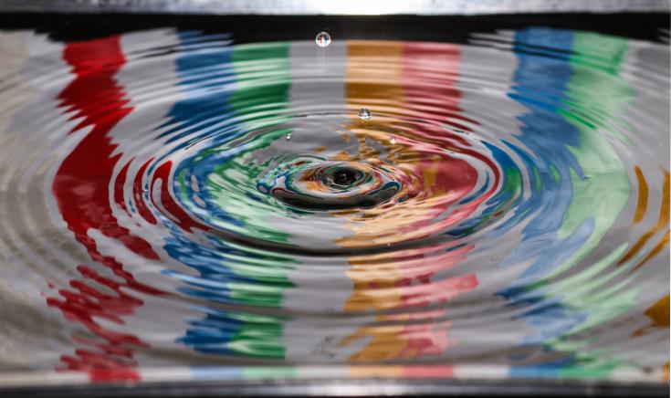 Drop of water falling into water reflecting colours