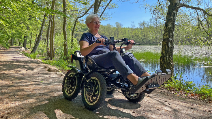 A woman with white short hair on a wheelchair visits a green area on a sunny day