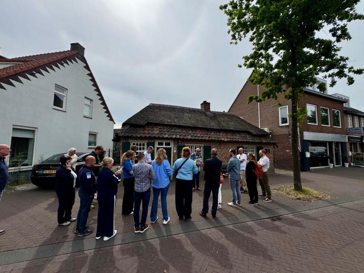 Group of people facing away from the camera are standing in the street in front of houses. 