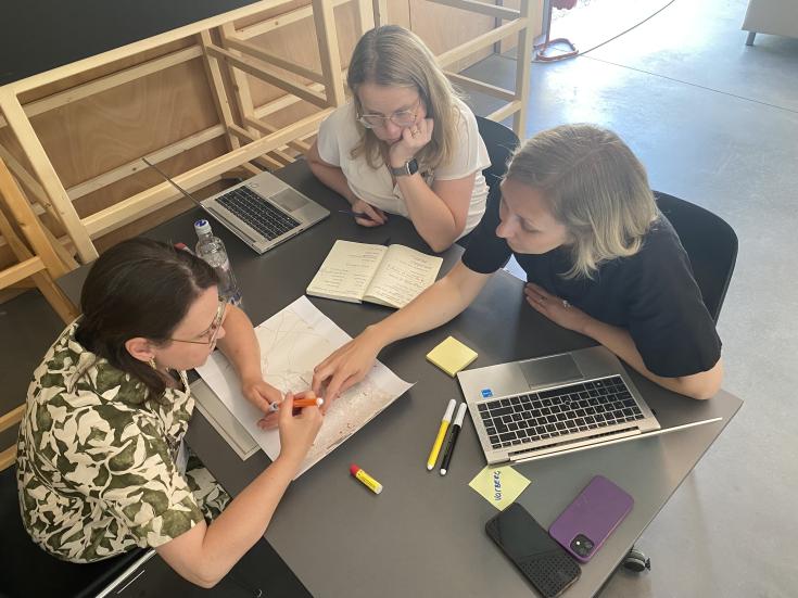 Three people sitting around a table examining map Three people sitting around a table examining map