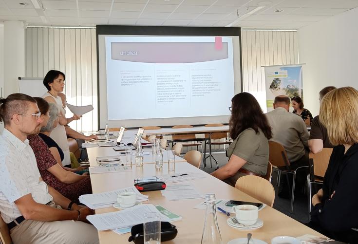 A group of people in a meeting room with a big screen displaying a powerpoint presentation