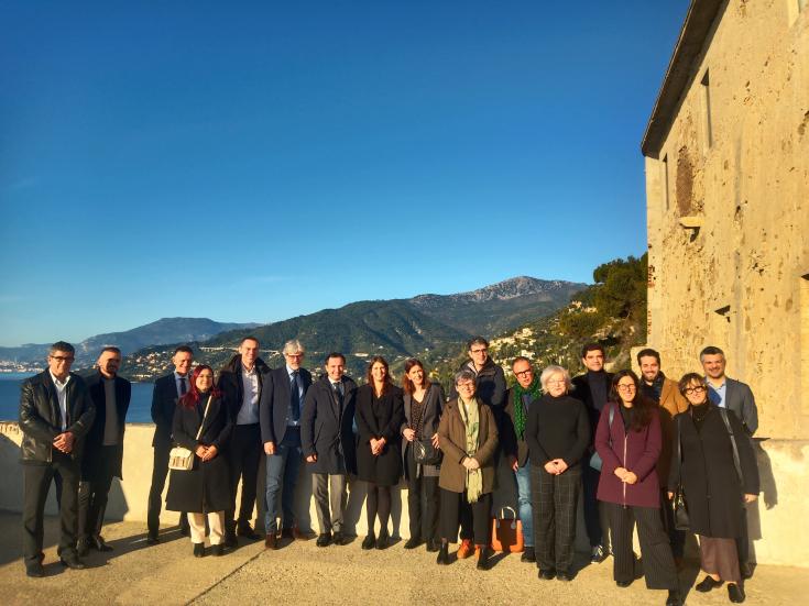 Around 20 people are gathered in front of the sea and moutains