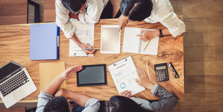 People sit around a desk with paper